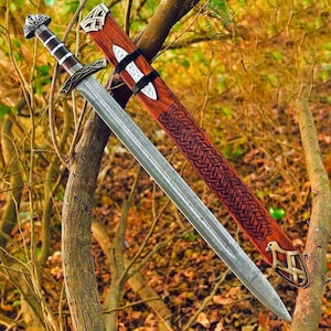 May include: A steel sword with a patterned blade and a dark handle featuring a metallic pommel and crossguard. The accompanying wooden scabbard displays intricate carved knotwork patterns and a metallic tip shaped like a bird head.