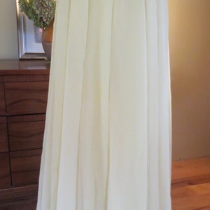 May include: A long, flowing, pale yellow skirt. The skirt is made of a lightweight, sheer fabric that drapes elegantly. It features a pleated design at the waist, creating a full, A-line silhouette. The skirt is displayed on a mannequin.