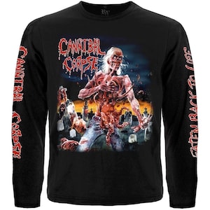 Puede incluir: Una camiseta negra de manga larga con un gráfico de un zombi en un cementerio y el texto Cannibal Corpse. Las mangas tienen el texto Cannibal Corpse a la izquierda y Eaten Back to Life a la derecha en una fuente roja de estilo goteante.