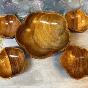 May include: A set of five wooden bowls with a smooth, polished finish and a distinct flower-like shape. The collection includes one large central bowl surrounded by four smaller matching bowls, all featuring visible natural wood grain patterns.