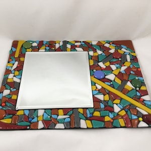 May include: A rectangular mirror with a mosaic tile frame. The frame features a colorful arrangement of red, yellow, green, blue, and gray tiles. The mirror is square and centered within the frame, creating a decorative piece.