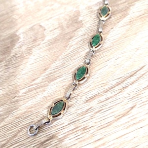May include: A silver-toned link bracelet featuring six marquise-shaped green stone inlays. Each stone is set within a metallic frame with a textured border, connected by small silver-toned metal bars to form a continuous chain design.