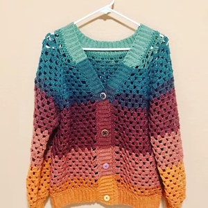 Könnte beinhalten: Eine langärmelige Häkelstrickjacke mit V-Ausschnitt und Knopfleiste. Das Kleidungsstück zeigt ein horizontales Farbblockmuster in den Tönen Hellgrün, Türkis, Dunkellila, Kastanienbraun, Altrosa und Orange mit unterschiedlich gestalteten Knöpfen.