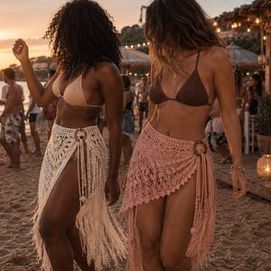 Peut inclure: Deux paréos en crochet avec des détails à franges et un anneau en bois circulaire au niveau de la hanche. L'un est de couleur crème avec un motif ajouré complexe, tandis que l'autre est rose poudré avec un tricot en dentelle délicat.