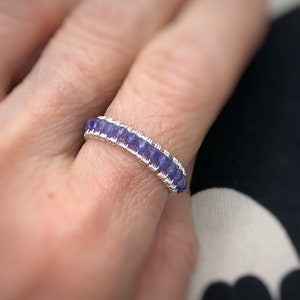 May include: A silver wire wrapped ring with a row of small, purple gemstones.