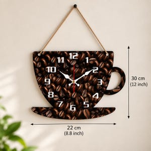 May include: A coffee cup-shaped wall clock featuring a dark brown roasted coffee bean pattern, white numerals, and white clock hands. The clock hangs from a brown rope and measures 30 cm (12 inches) in height and 22 cm (8.8 inches) in width.