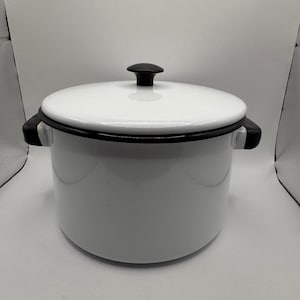 May include: A white enamel stockpot with a matching lid, featuring a black rim and two black side handles. The lid is topped with a small, rounded black knob. The pot has a cylindrical body and a smooth, glossy finish throughout the exterior.