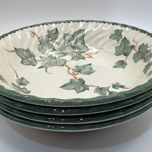 May include: A stack of four round ceramic bowls with a cream-colored base and a scalloped edge. The interior of each bowl features a green ivy leaf pattern with brown vine accents, and the rim is finished with a textured dark green border.