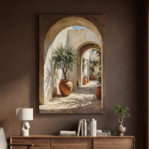 May include: A rectangular wall art print depicting a sunlit Mediterranean courtyard with stone arches, terracotta pots containing olive trees, and climbing vines. The scene features warm beige and brown tones, stone flooring, and deep shadows.