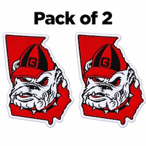 Peut inclure: Un lot de 2 écussons brodés représentant le contour de l'État de Géorgie en rouge, avec un bouledogue blanc portant une casquette rouge et noire avec un G, et un collier à pointes. Le texte Pack of 2 est visible au-dessus.