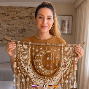 Könnte beinhalten: Ein Wandbehang mit einem Ast aus Naturholz als Basis, an dem cremefarbene Makramee-Kordeln in komplexen Mustern hängen. Ein goldfarbener Halbmond ist mit klaren Kristallen und Perlen besetzt und mit hängenden Kristalltropfen verziert.