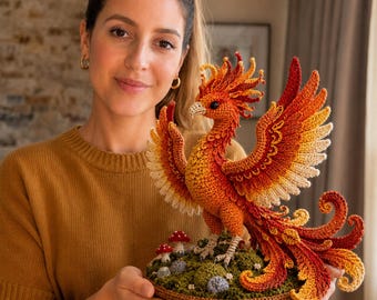 Può includere: Una statuetta di fenice realizzata all'uncinetto a mano con piumaggio in filato rosso, arancione e giallo vivace, ali spiegate e una lunga coda arricciata. L'uccello mitico poggia su una base verde testurizzata decorata con piccoli funghi.