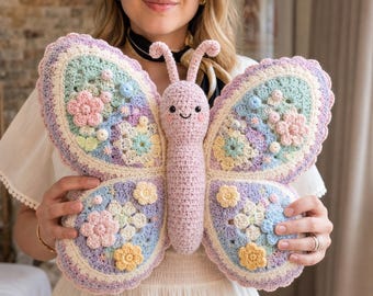 Può includere: Un grande peluche a forma di farfalla realizzato a mano all'uncinetto, con un corpo centrale rosa tenue, un viso sorridente e antenne. Le ali sono create in una palette di colori pastello azzurro, lavanda, verde menta e giallo, decorate con piccoli fiori 3D.