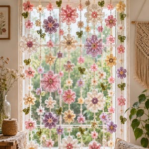 Puede incluir: Una cortina de ventana compuesta por múltiples hilos verticales de flores de ganchillo en tonos rosa, morado, amarillo y blanco, intercalados con pequeñas hojas verdes de ganchillo. Los hilos florales cuelgan de una barra horizontal.