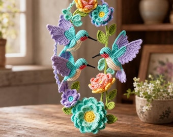 Può includere: Una giostrina all'uncinetto da appendere con tre colibrì dai corpi color ottanio, viola e crema con gole rosse. Gli uccelli sono circondati da fiori all'uncinetto nelle tonalità del giallo, rosa, viola e ottanio, insieme a foglie e viticci verdi.