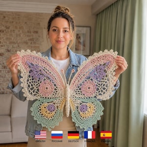 May include: A large, intricate crochet butterfly wall hanging featuring a cream-colored base with pastel accents in pink, lavender, yellow, and mint green. The design includes detailed openwork patterns, scalloped edges, and two thin antennae.