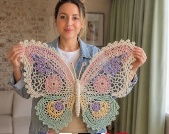 May include: A large, intricate crochet butterfly wall hanging featuring a cream-colored base with pastel accents in pink, lavender, yellow, and mint green. The design includes detailed openwork patterns, scalloped edges, and two thin antennae.