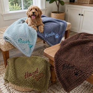 May include: Four soft, textured waffle-knit blankets in light blue, dark blue, olive green, and brown. Each blanket is personalized with embroidered names: Buddy with a heart, Koda with a paw print, Hazel with a bone, and Blue with a paw print.