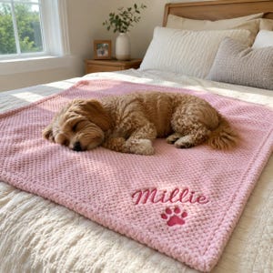 Peut inclure: Une couverture texturée rose clair douce avec le prénom Millie brodé en écriture cursive, accompagné d'une petite icône de patte brodée. La couverture est rectangulaire et présente un motif de tissu gaufré sur toute sa surface.