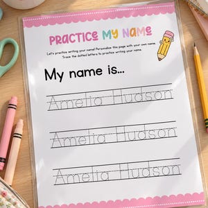 Puede incluir: Una hoja de práctica plastificada con un borde festoneado rosa que presenta el texto Practice My Name y My name is... con tres líneas de letras punteadas que deletrean Amelia Hudson y un dibujo de un lápiz en la esquina superior derecha.