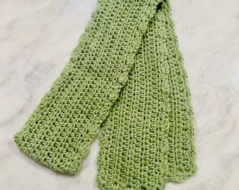 Könnte beinhalten: Ein salbeigrüner Schal mit einem strukturierten Häkelstichmuster. Der Schal hat eine gleichmäßige rechteckige Form mit gewellten Kanten an den Seiten und Enden und weist eine einheitliche Strickkonstruktion über die gesamte Länge des Artikels auf.