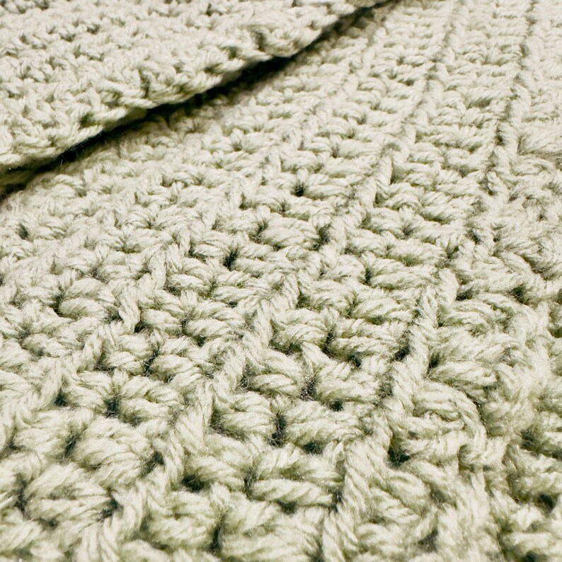 K&ouml;nnte beinhalten: Ein helles, salbeigr&uuml;nes geh&auml;keltes Textil mit einem dichten, sich wiederholenden Stichmuster. Der Stoff weist eine konsistente, strukturierte Oberfl&auml;che auf, die durch ineinandergreifende Garnschlaufen entsteht und eine einheitliche Farbe zeigt.