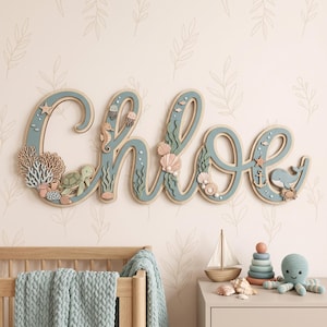 May include: A wall-mounted wooden name sign spelling Chloe in cursive script, featuring a dusty blue finish and layered ocean-themed cutouts including a sea turtle, seahorse, jellyfish, coral, seashells, an anchor, and a whale.