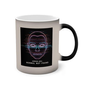 Könnte beinhalten: Ein matter, hellgrauer Becher mit schwarzem Henkel und einer schwarzen, rechteckigen Grafik auf der Vorderseite. Die Grafik zeigt ein stilisiertes menschliches Gesicht mit horizontalen rosa und blauen Glitch-Linien und dem Text ERROR 404: NORMAL NOT FOUND.