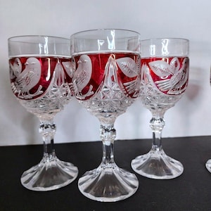 Könnte beinhalten: Drei Kelchgläser aus klarem und rubinrotem Glas mit geätzten Vogel- und Blattmotiven. Die Kuppen haben ein tiefrotes Band mit mattierten Vögeln, während die unteren Bereiche und Stiele ein klares, komplexes Diamantschliffmuster aufweisen.