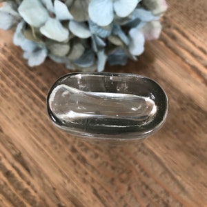 Puede incluir: Una botella de vidrio transparente con una parte superior redondeada y una superficie lisa ligeramente texturizada.