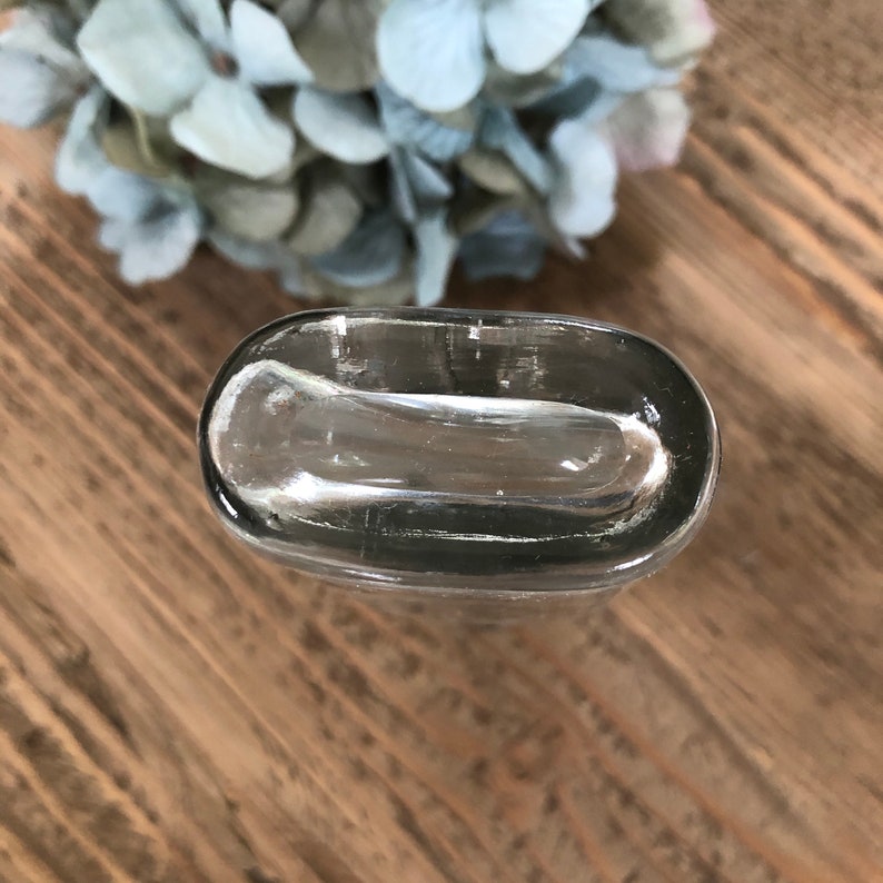 Puede incluir: Una botella de vidrio transparente con una parte superior redondeada y una superficie lisa ligeramente texturizada.