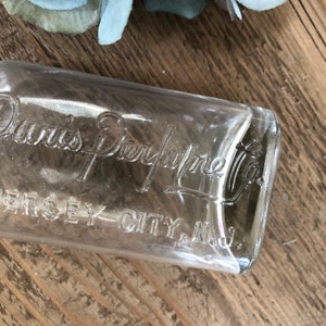 Puede incluir: Una botella de vidrio transparente con una etiqueta que dice "Davis Perfume Co. Jersey City, N.J."