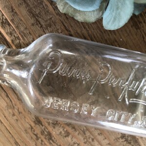 Puede incluir: Una botella de vidrio transparente con el texto "Davis's Dry-Lye" y "Jersey City, N.J." en relieve en el lateral.