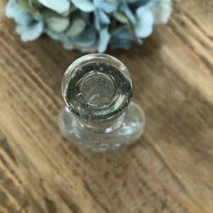 Puede incluir: Una botella de vidrio transparente con una abertura redonda y una superficie texturizada. La botella est&aacute; vac&iacute;a y parece ser vintage.