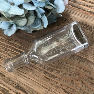 Puede incluir: Una botella de vidrio transparente con una superficie texturizada. La botella est&aacute; etiquetada con "Merck & Co. Inc.  5 cc.  Dosage Bottle".