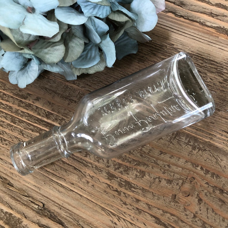 Puede incluir: Una botella de vidrio transparente con una superficie texturizada. La botella est&aacute; etiquetada con "Merck & Co. Inc.  5 cc.  Dosage Bottle".