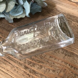 Puede incluir: Una botella de vidrio transparente con el texto "Duvis Perfume Co. Jersey City N.J." grabado en el lateral.