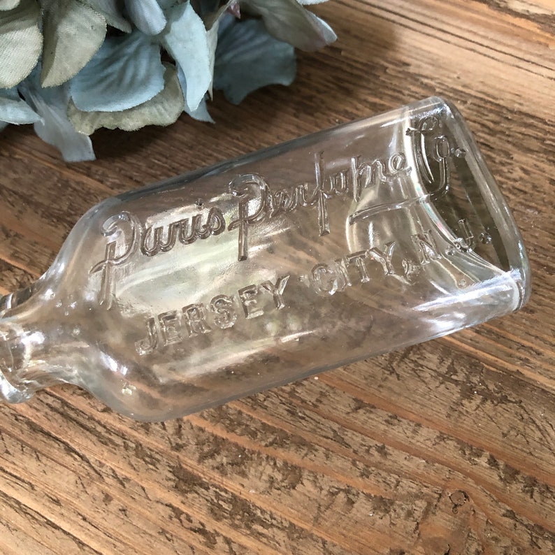 Puede incluir: Una botella de vidrio transparente con el texto "Duvis Perfume Co. Jersey City N.J." grabado en el lateral.