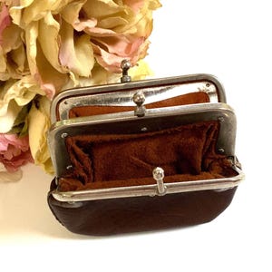 May include: A small, dark brown leather coin purse featuring a silver-toned metal frame with a kiss-lock closure. The interior is lined with a soft, matching brown suede material. The frame has two distinct metal ball clasps for opening.