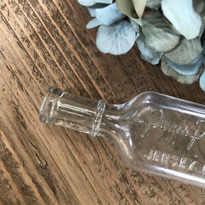 Puede incluir: Una botella de vidrio transparente con una superficie texturizada. La botella tiene una etiqueta que dice "Davis's Pharmacy Jersey City".