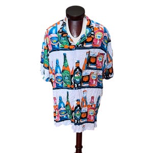 May include: A short-sleeved button-down shirt with a white background and a colorful print of various beer bottles and cans. The shirt has a collared neckline and is displayed on a mannequin.