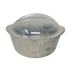 May include: A silver cast iron pot with a glass lid. The lid has a floral design etched into it.