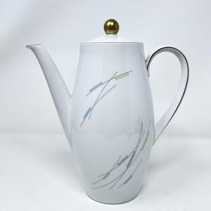 May include: White ceramic coffee pot with a gold lid and a geometric design in shades of blue, yellow, and purple.