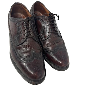 May include: A pair of brown leather wingtip shoes with a brogue pattern. The shoes have laces and are in good condition.
