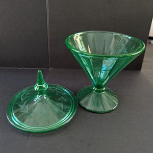 May include: A vibrant green glass candy dish with a matching lid. The bowl features a wide, flared rim and a pedestal base. Both the lid and the bowl are decorated with a delicate, etched leaf pattern that encircles the glass surface.