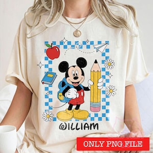 Pode incluir: Uma t-shirt de cor creme com um gráfico do Mickey Mouse a segurar um lápis amarelo grande e a usar uma mochila azul. O design inclui uma maçã vermelha, um livro azul, um avião de papel, margaridas e o nome WILLIAM em texto preto.