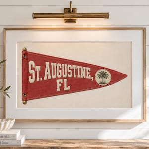 Könnte beinhalten: Ein roter dreieckiger Wimpel mit dem weißen Text ST. AUGUSTINE, FL und einem kreisförmigen Emblem mit einer Palmenillustration. Der Wimpel hat zwei messingfarbene Ösen an der linken Seite und ist in einem rechteckigen Holzrahmen gerahmt.