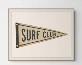 May include: A framed wall art print featuring a triangular pennant with a weathered cream-coloured fabric base. The pennant displays the black text SURF CLUB and includes a dark vertical strip on the left side with two brass-coloured metal grommets.