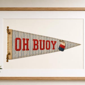 May include: A triangular pennant featuring a blue and white vertical striped pattern with the red text OH BUOY printed in the centre. A small tag shaped like a buoy with red, white, and blue horizontal stripes hangs from the right side of the fabric.