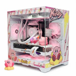 May include: A custom desktop computer case featuring a pink and white striped theme with Kirby character graphics and text. The interior includes white components, pink LED fans, a GeForce RTX graphics card, and two small Kirby figurines inside.